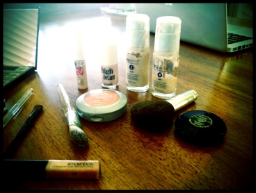 Makeup Bag Essentials From left: foundation applicator brush, concealer, highlighter, foundation, blush, blush/powder brush, powder, and lip gloss.